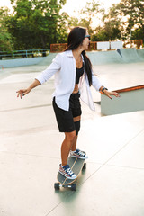 Photo of pretty young woman smiling while riding skateboard in skate park