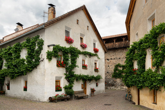 A very old white house with red flowers and vine in Glurns