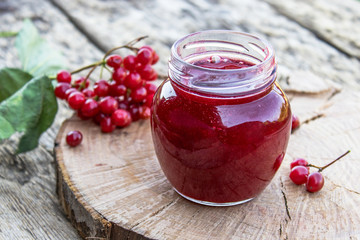 Viburnum fruit jam in a glass jar on a wooden table near the ripe red viburnum berries. Source of natural vitamins. Used in folk medicine.
