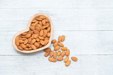 Almond nuts on heart shape wooden bowl on white wooden,top view