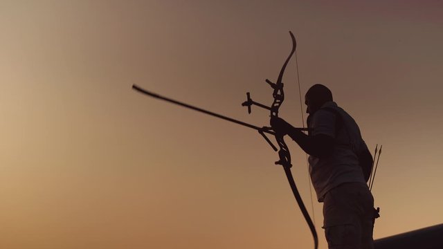 Archery silhouette, sun sets behind the archer. Man shoots a bow
