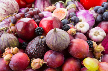 Background of fresh vegetables and fruits. Purple eggplant, plums, figs, apples, avocado, grape, hazelnut, sweet pepper, tomato and garlic. Purple and red food. Different vegetables on the table.