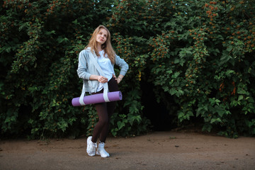 Fitness woman carrying yoga mat with strap on vegetative background