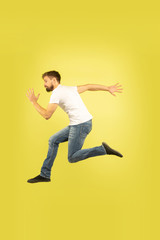 Fototapeta na wymiar Full length portrait of happy jumping man isolated on yellow background. Caucasian male model in casual clothes. Freedom of choices, inspiration, human emotions concept. Run for sales, hurry up.
