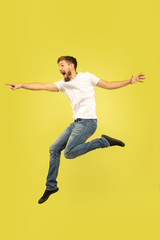 Fototapeta na wymiar Full length portrait of happy jumping man isolated on yellow background. Caucasian male model in casual clothes. Freedom of choices, inspiration, human emotions concept. Pointing, choosing.
