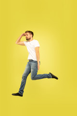 Full length portrait of happy jumping man isolated on yellow background. Caucasian male model in casual clothes. Freedom of choices, inspiration, human emotions concept. Run for sales, hurry up.