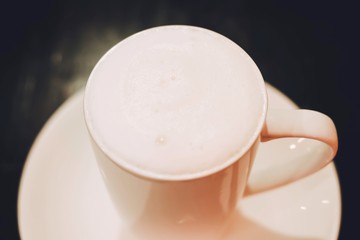 Hot milk in white ceramic cup on the wooden table.