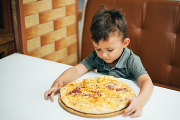 a little boy in a cafe or pizzeria sitting on the couch on the table on the stand a whole pizza,...
