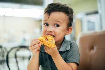 a little boy in a cafe or pizzeria sitting on the couch at the table and eats a piece of cut pizza,...