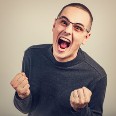 Angry young man shouting with open mouth and very anger face, showing the fists in fashion glasses