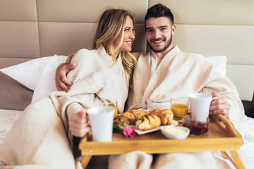 Obraz na płótnie Canvas Young happy couple having breakfast in luxury hotel room