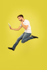 Full length portrait of happy jumping man isolated on yellow background. Caucasian male model in casual clothes. Freedom of choices, inspiration, human emotions concept. Takes video for vlog or