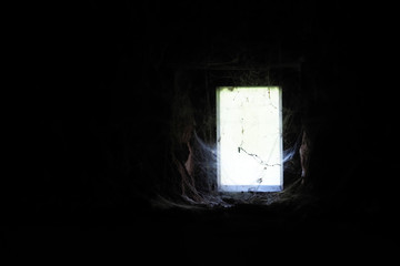 Dungeon, darkness, a narrow small window twisted by a spider web. Horror concept