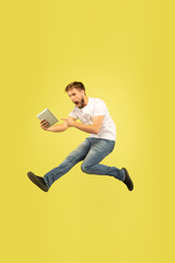 Full length portrait of happy jumping man isolated on yellow background. Caucasian male model in casual clothes. Freedom of choices, inspiration, human emotions concept. Takes video for vlog or