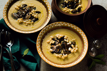 mushroom soup with Italian cannellini beans and fennel in clay pots on a table. Autumn healthy vegan food. top shot