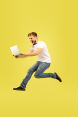 Full length portrait of happy jumping man isolated on yellow background. Caucasian male model in casual clothes. Freedom of choices, inspiration, human emotions concept. Using tablet in flight.