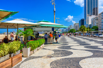 View of Copacabana beach with palms and mosaic of sidewalk in Rio de Janeiro, Brazil. Copacabana beach is the most famous beach in Rio de Janeiro. Sunny cityscape of Rio de Janeiro