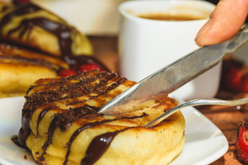 Pancakes with strawberries chocolate and coffee on a wooden table
