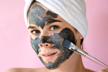 Young woman apply clay facial mask. Face peeling mask with charcoal, spa beauty treatment, skincare, cosmetology. Close up