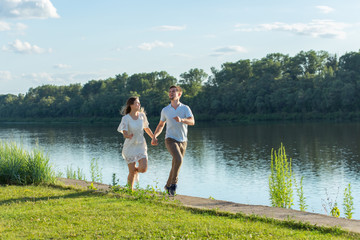 Fototapeta na wymiar Summer nature, relationship and people in love concept - happy couple running near the lake