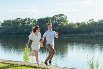 Summer nature, relationship and people in love concept - happy couple running near the lake