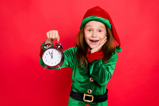 Close-up portrait of her she nice attractive cheerful cheery amazed delighted glad funny pre-teen elf holding in hands clock twelve midnight isolated over bright vivid shine red background