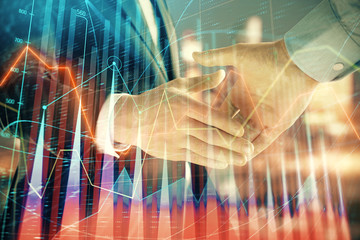 Double exposure of financial chart on cityscape background with two businessmen handshake. Concept of financial analysis and investment opportunities