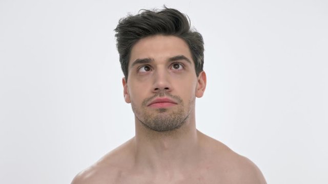 Close up view of young brunette man with naked torso looking up with crossed eyes and fixing his hairstyle with hand over white background isolated