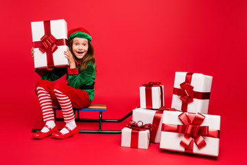 Nice attractive cheerful cheery glad excited funny pre-teen elf sitting on sled holding in hands...