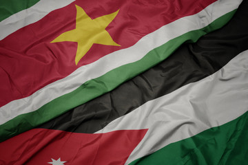 waving colorful flag of jordan and national flag of suriname.