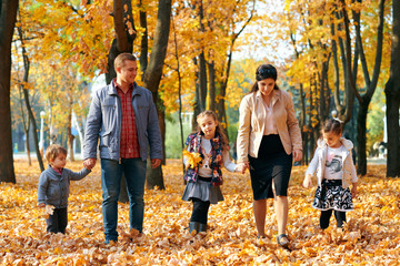 Happy family having holiday in autumn city park. Children and parents posing, smiling, playing and having fun. Bright yellow trees and leaves