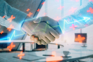 Multi exposure of heart icon hologram on office background with two men handshake. Concept of medical education