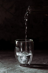 Water poured from the bottle into a glass cup on a black background