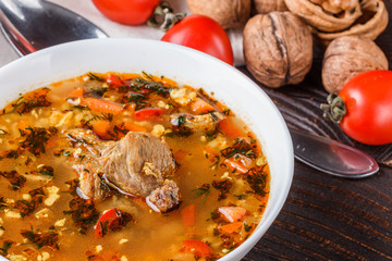 Georgian soup. Kharcho with rice, tomato, beef, garlic and herbs in bowl on wooden table