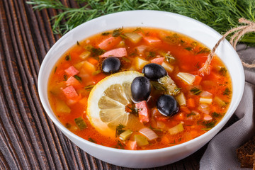 Traditional Russian meat soup Solyanka in bowl on rustic wooden table