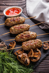 Shish kebab on the skewers with sauce, grilled mushrooms on rustic table