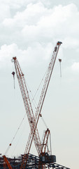 Fototapeta premium Boom cranes at a construction site against the sky and clouds. Vertical rectangular image.