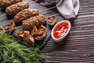 Shish kebab on the skewers with sauce, grilled mushrooms on rustic table
