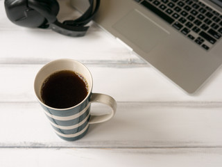 White wooden working desk with laptop, headphones and large mug of coffee.