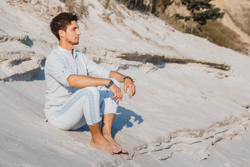 Young handsome man in light clothing sits in the desert. Concept of freedom relaxation. Place for text or advertising