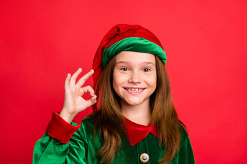 Close up photo of charming elf kid in green hat with long red head haircut showing ok sign...
