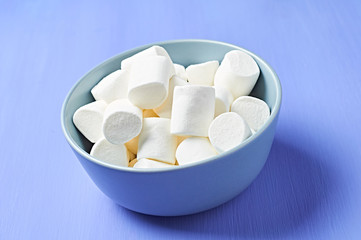 Full gray ceramic bowl of sugary white marshmallow cylindrical form on purple scratched concrete table. Close-up