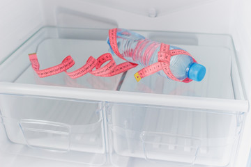Empty refrigerator with a bottle of water and pink tape measuring on the shelf inside, diet concept