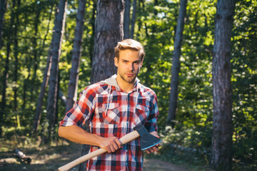 Naklejka na ściany i meble Illegal logging continues today. Logging. Agriculture and forestry theme. Strong man lumberjack with an ax in a plaid shirt. Handsome man lumberjack with a large ax examines the tree before felling.
