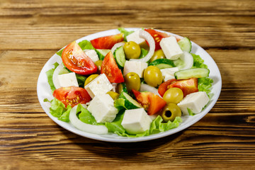 Greek salad with fresh vegetables, feta cheese and green olives on wooden table