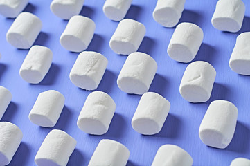 Many rows of white marshmallows cylindrical form lies on purple scratched concrete table. Pattern