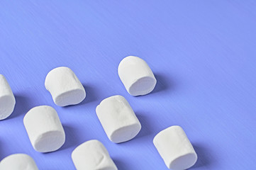 Rows of white marshmallows cylindrical form lies on purple scratched concrete table. Space for text