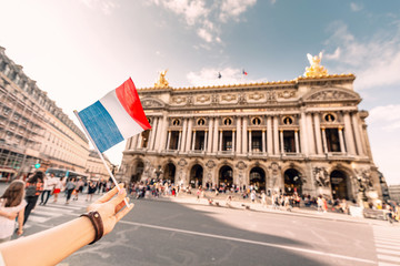 Obraz premium happy Asian girl traveler with french flag near the main Facade of the Opera Garnier in the historic building of the Academy of music of Paris. The concept of Sights and cultural attractions of France