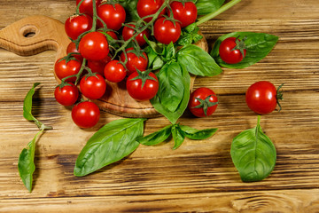 Fresh cherry tomatoes with green basil leaves on a wooden table