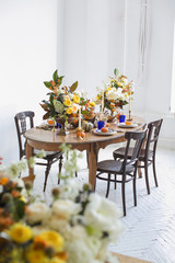 Luxurious elegant wedding decor in autumn style. Wooden vintage table and chairs setting with ceramic plates and silver cutlery. Fresh flowers in a vase, orange pumpkins, deer horns and candles.